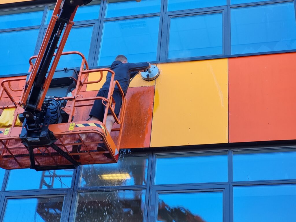 Medarbejder fra Q-Clean udfører facadevask på erhvervsbygning med lift.