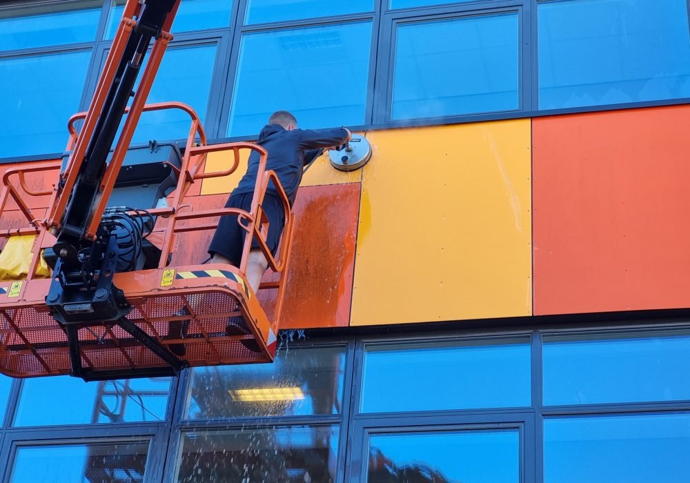 Medarbejder fra Q-Clean udfører facadevask på erhvervsbygning med lift.
