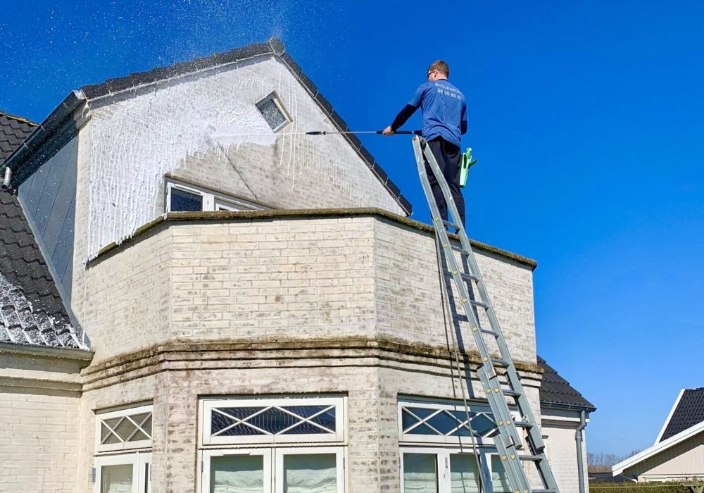 Medarbejder fra Q-Clean udfører facaderens på bygning fra stige.